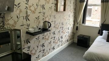 A bedroom with floral wallpaper, a bed, a bedside table, a mirror, and a window with curtains.