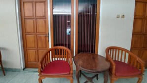 A room with two wooden chairs with red cushions, a small round table, and a wooden door with a window above it. - Hotel Sri Timur (Yogyakarta)