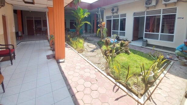 A covered outdoor area with hexagonal tiles, a seating area with chairs, and a small garden with plants and a decorative water feature. - Hotel Sri Timur (Yogyakarta)