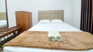 A hotel room with a bed, a wooden wardrobe, a mirror, and a curtain. - Hotel Sri Timur (Yogyakarta)