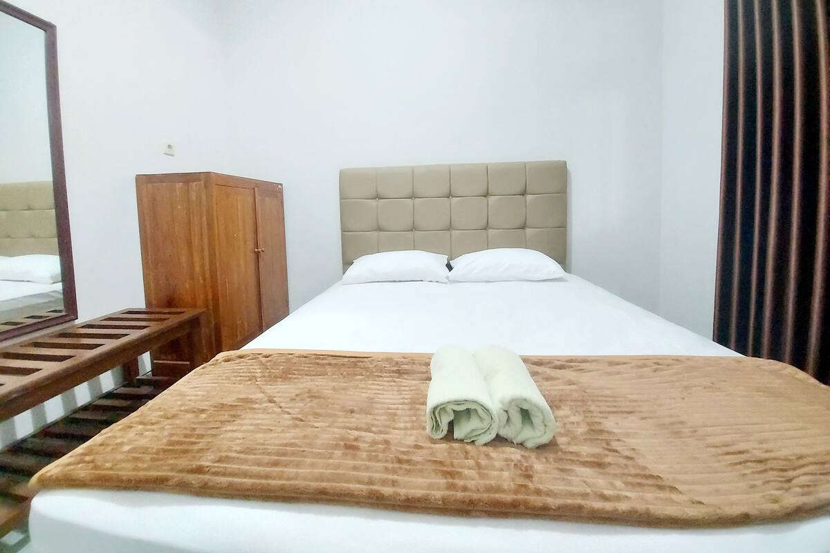A hotel room with a bed, a wooden wardrobe, a mirror, and a curtain.