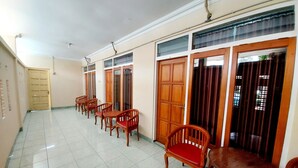 A hallway with wooden doors, a tiled floor, and several wooden chairs. - Hotel Sri Timur (Yogyakarta)