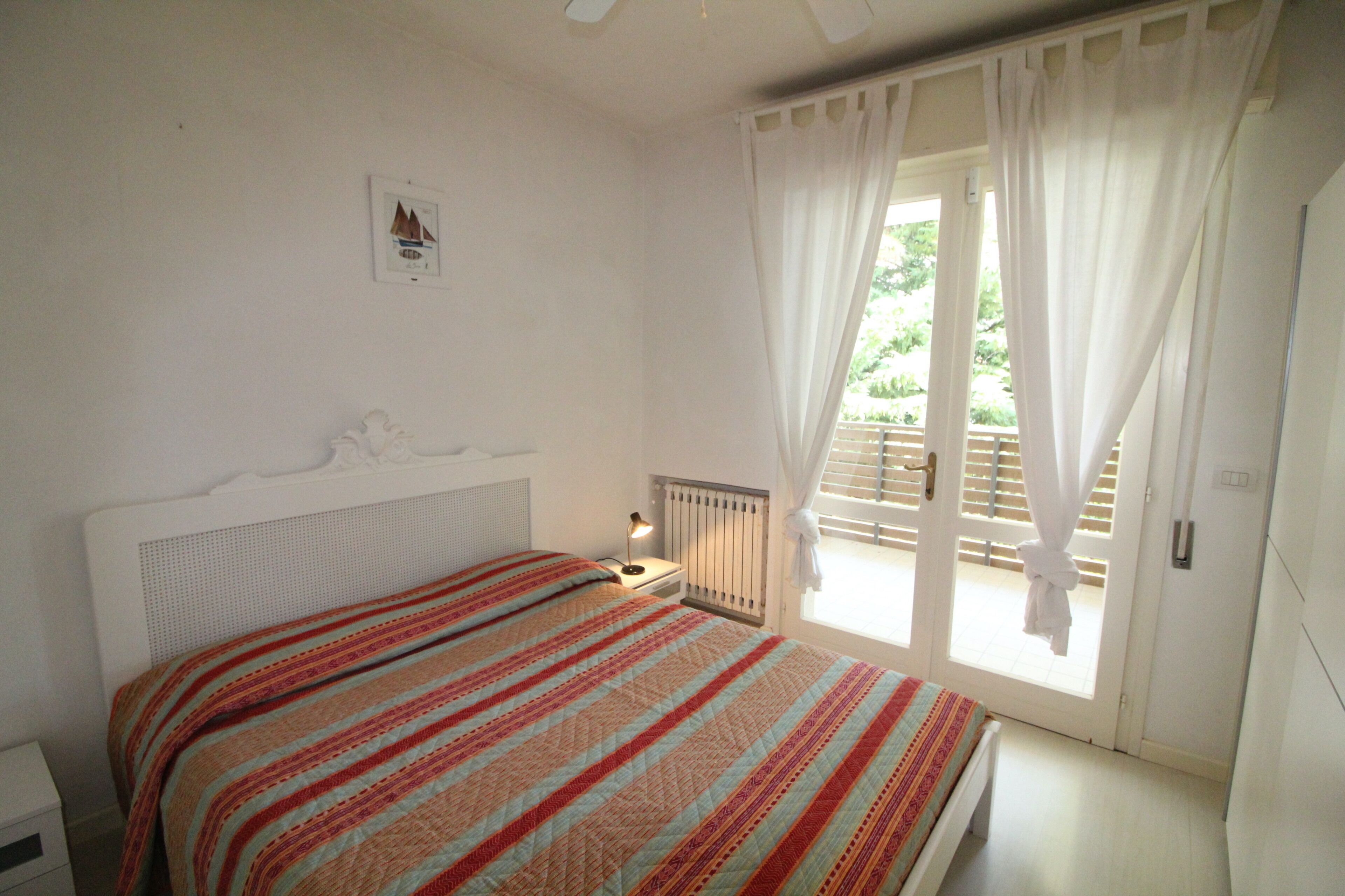 A bedroom with a bed, a nightstand, a window with curtains, and a radiator.