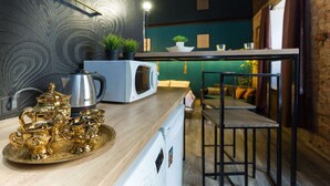Une cuisine équipée d’un four à micro-ondes, d’une bouilloire et d’un service à thé, le tout disposé sur un plateau. On y trouve également un coin bar avec des tabourets et, au fond, un mur vert.