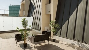 An outdoor seating area with chairs and potted plants, a modern building with a sloped roof, and a construction crane in the background. - Dec Apartments (Bucharest)