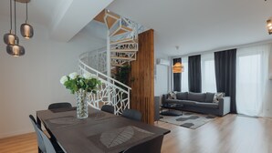 A modern living room with a grey sofa, a wooden staircase, and a dining area with a dark wooden table and chairs. - Dec Apartments (Bucharest)