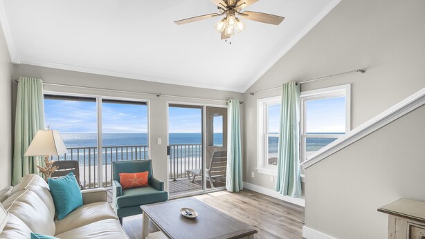 Ein geräumiges Wohnzimmer mit großem Fenster zum Meer, einem Deckenventilator und einem Holztisch.