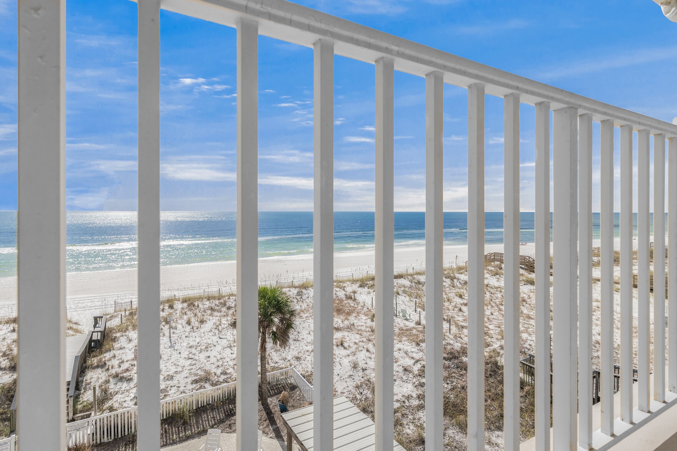 Blick auf einen Strand vom Balkon mit weißen Geländern, feinem Sand und dem Meer.
