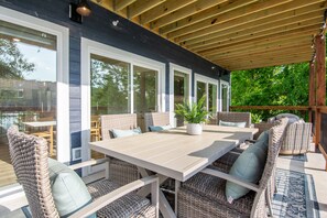 An outdoor patio with a table and wicker chairs, large windows, and a wooden ceiling. - Lakefront, Private Hot Tub, By Downtown Landing | Mini Pearl (Branson)