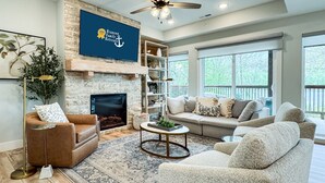 A living room with a stone fireplace, a ceiling fan, and a large window overlooking a deck. - Lakefront, Private Hot Tub, By Downtown Landing | Mini Pearl (Branson)