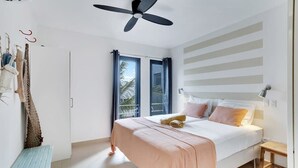 A bedroom with a bed, a ceiling fan, a window with curtains, a bench, and a wall-mounted light fixture.