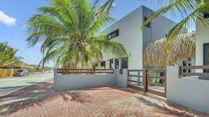 A modern building with a brick-paved entrance, a palm tree, and a thatched roof structure.