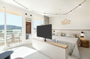 Una habitación de hotel moderna con una cama grande, un televisor en un mueble, un balcón con sillas y vistas a las colinas.