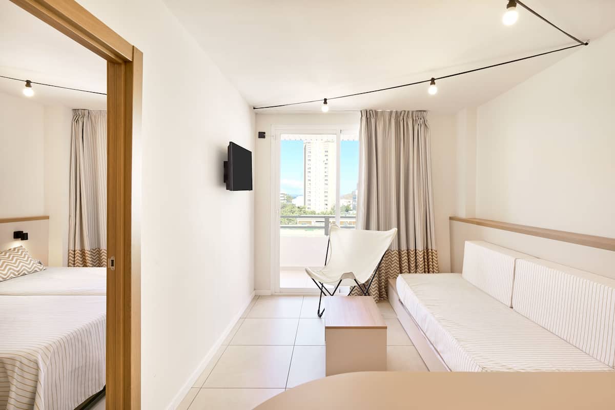 A modern hotel room with a bed, a sofa, a chair, a TV, and a balcony with curtains.