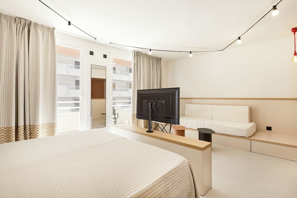 A hotel room with a large bed, a TV, a sofa, and a window with curtains.
