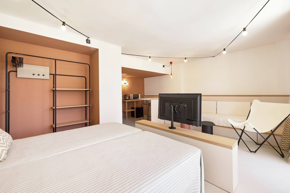 A modern bedroom with a bed, a desk with a computer, a chair, and a wardrobe.