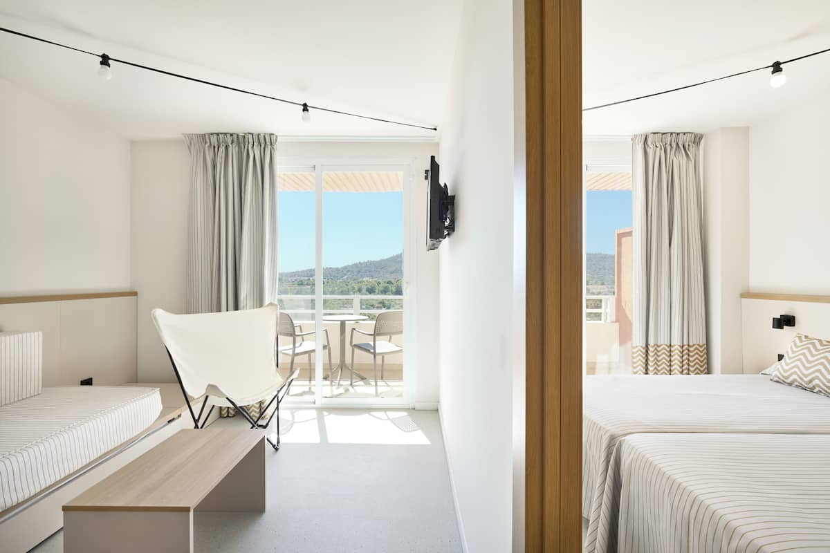 A hotel room with two beds, a small table, and a balcony with a view.