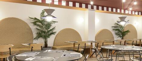 Un restaurante con mesas redondas, sillas de metal y diseños de pared con motivos.