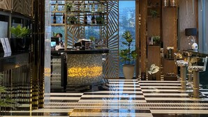 Um lobby moderno com piso xadrez, um balcão de recepção e vista da cidade através de amplas janelas.