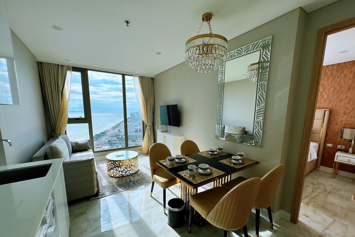 Una habitación de hotel moderna con zona de comedor, un espejo grande y vista al mar.