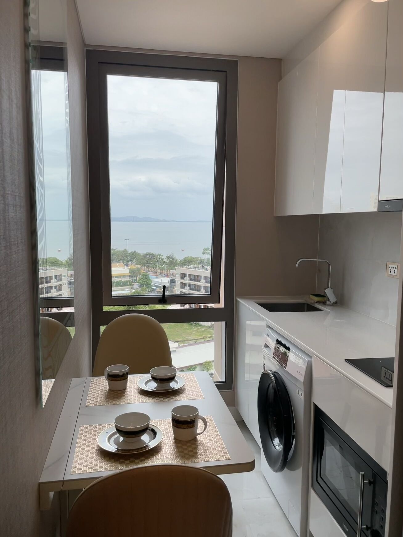 Een kleine keuken met uitzicht op zee, een wasmachine en een magnetron.