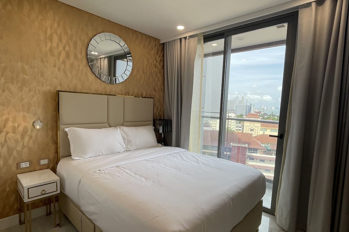 Una habitación de hotel moderna con una cama grande, un espejo redondo en la pared, una mesita de noche y vistas de la ciudad a través de la ventana.