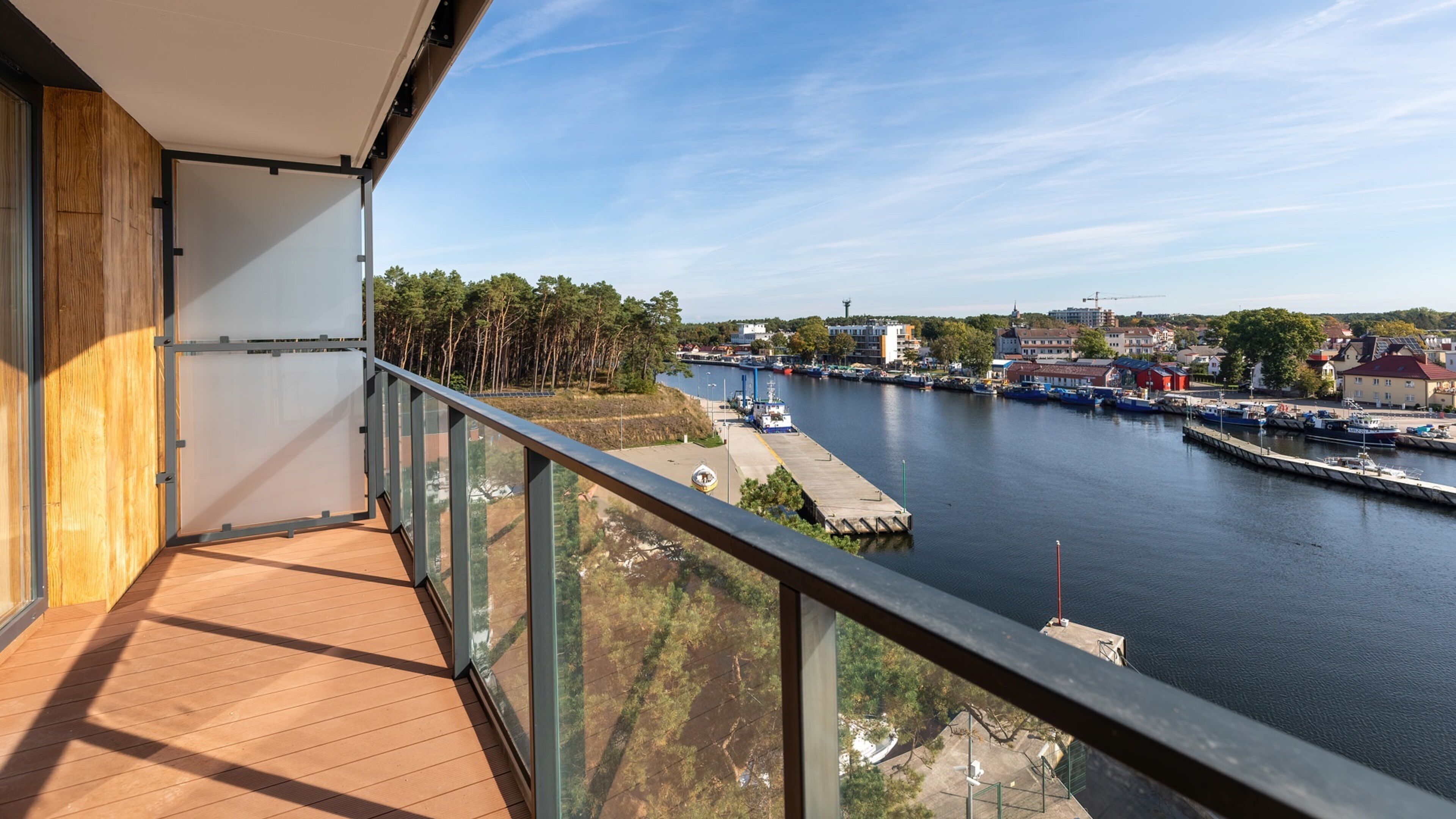 A balcony with a view of a river, docked boats, and buildings across the water.