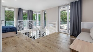 A modern bedroom with a balcony, wooden flooring, and large windows with curtains. - Apartamenty Sun & Snow Lighthouse (Trzebiatow)