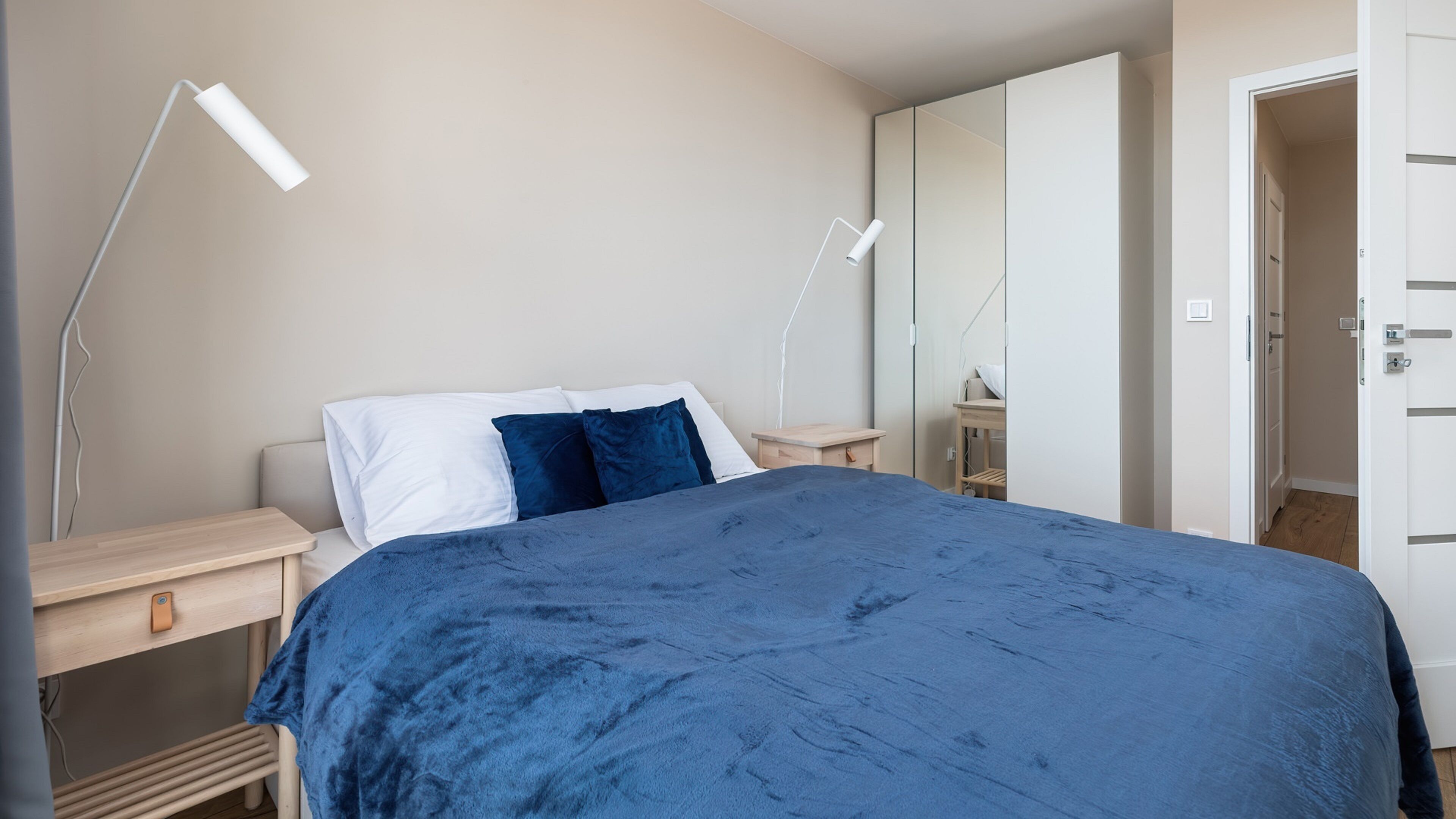 Un dormitorio con cama, mesitas de noche, armario y puerta.