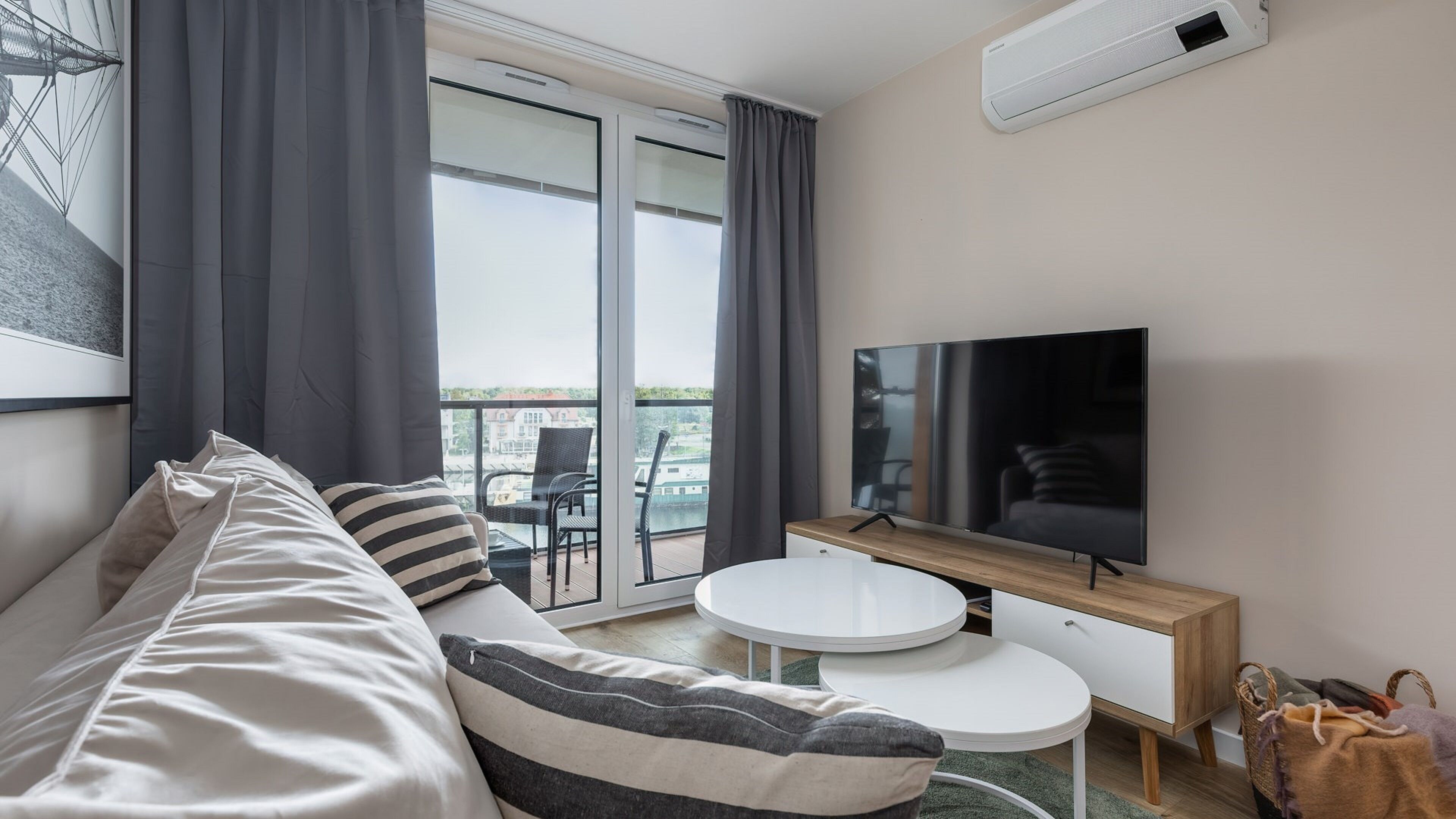 A modern hotel room with a sofa, a flat-screen TV, a small round table, and a balcony with a view.