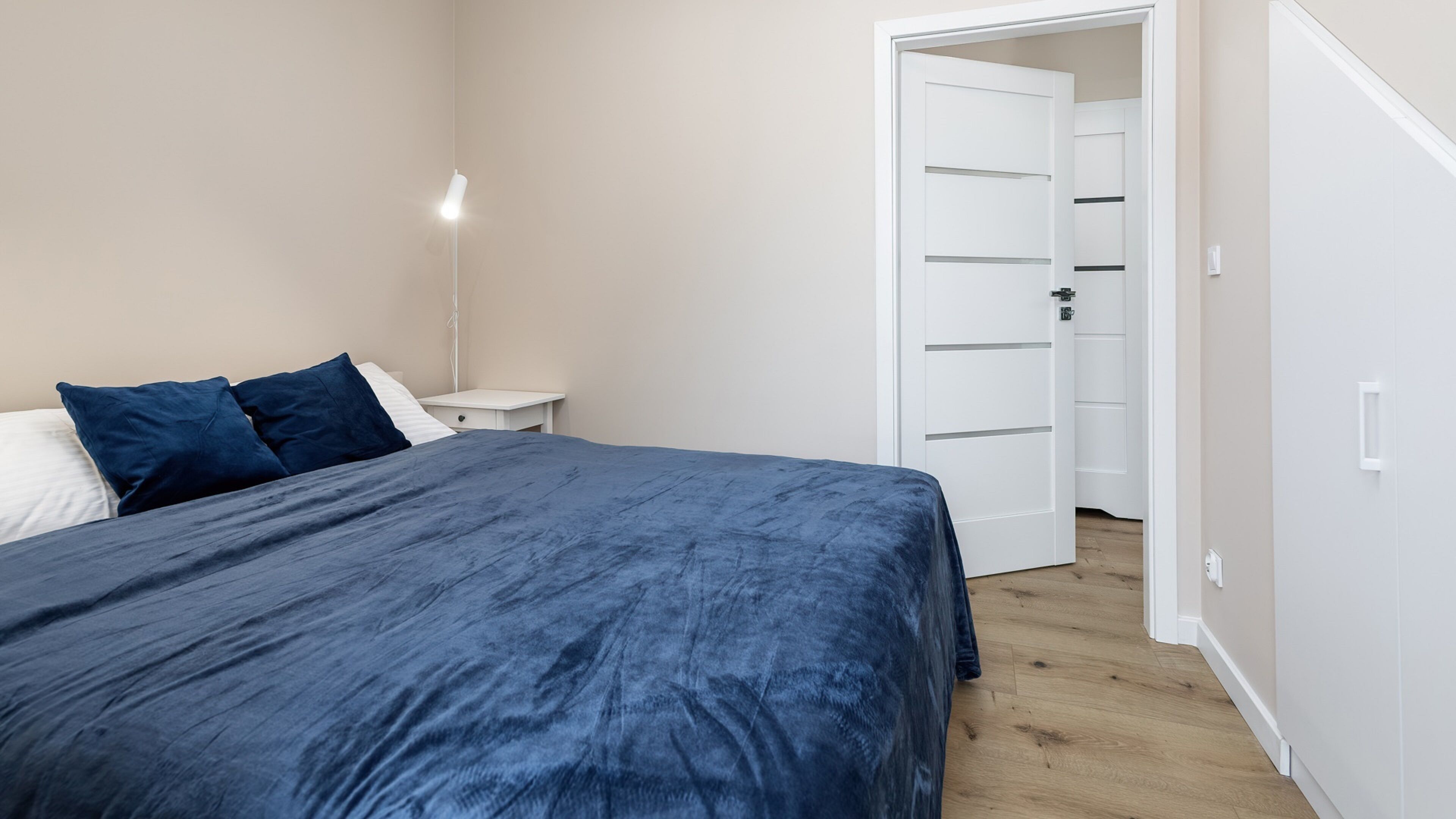 Et soveværelse med seng, natbord, lampe og et skab.