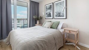 A modern bedroom with a large bed, a nightstand, a bedside table, and two framed pictures on the wall. - Apartamenty Sun & Snow Lighthouse (Trzebiatow)