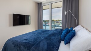 A hotel room with a bed, a flat-screen TV, a view of a harbor, and a balcony with curtains. - Apartamenty Sun & Snow Lighthouse (Trzebiatow)