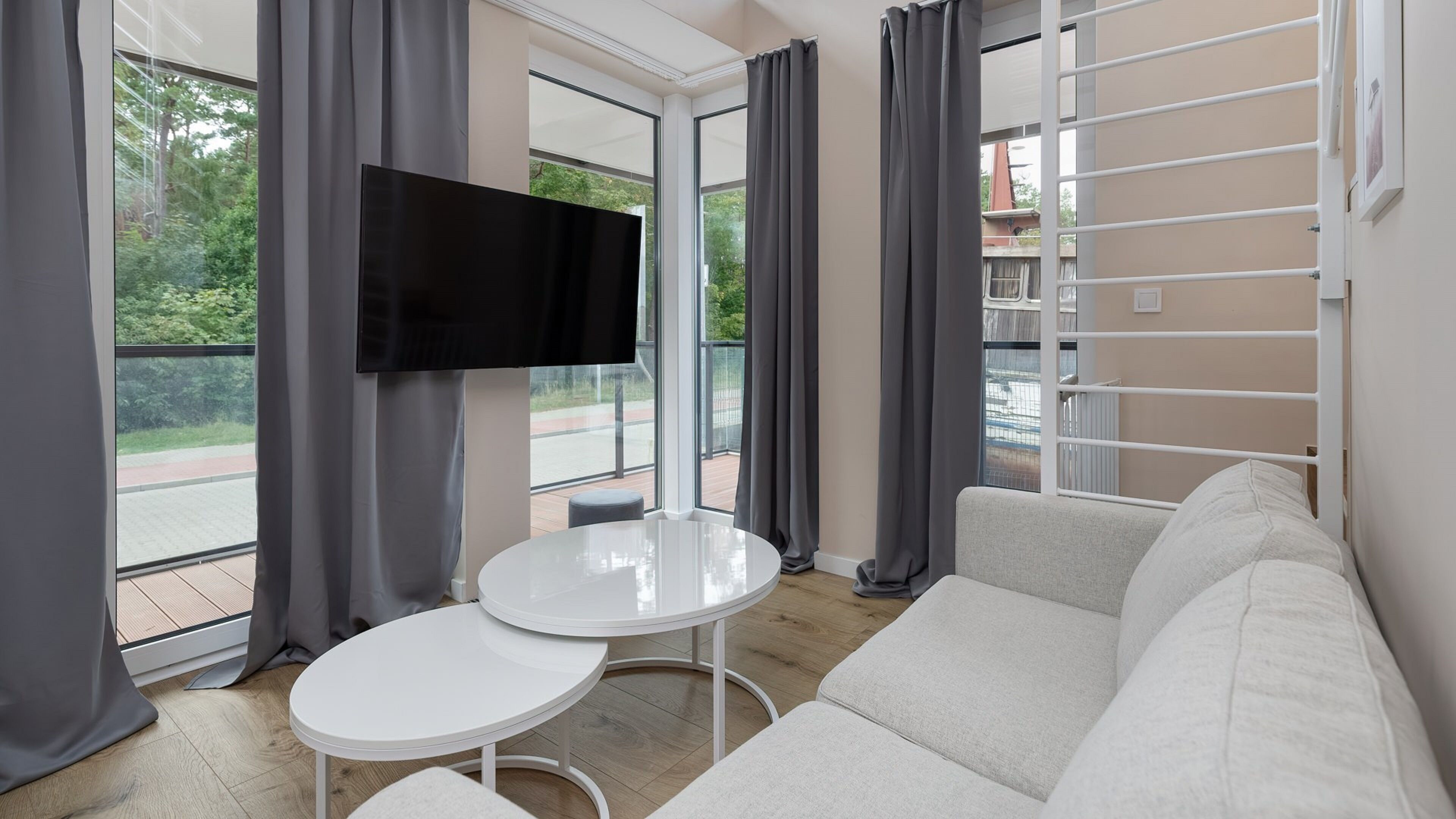 A modern living room with a white sofa, a small white table, and a flat-screen TV mounted on the wall.