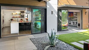 Una cocina moderna con una isla central, un comedor con barra y vistas a un paisaje urbano a través de puertas de cristal grandes.