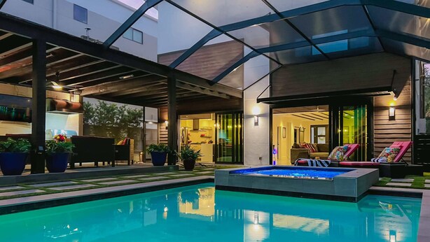 Un área de piscina exterior moderna con zona de estar techada y sillones reclinables.