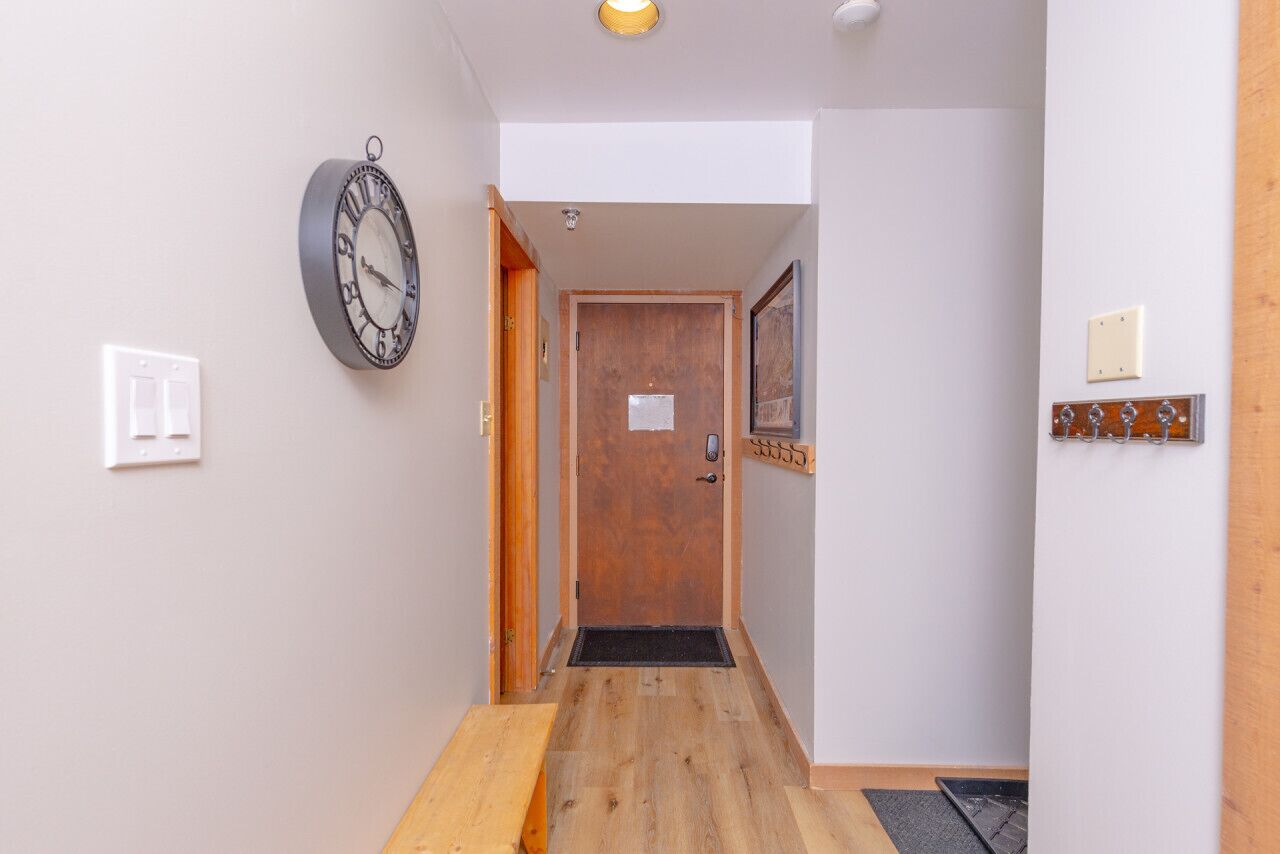 Un couloir avec un plancher en bois, une porte au fond et une horloge fixée au mur.