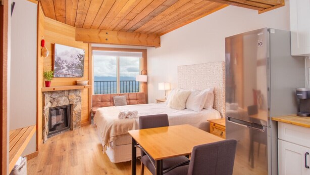 Une chambre confortable avec une cheminée en pierre, un lit avec des oreillers, une table en bois et un réfrigérateur moderne.