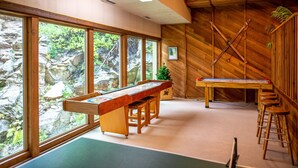 Une table de billard dans une pièce dotée de grandes fenêtres, de murs en bois et d’un plafond avec des poutres apparentes.