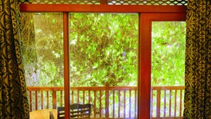 A room with a wooden bench, a table, and a view of lush green foliage through large glass doors. - Polhena Grand Resort (Matara)