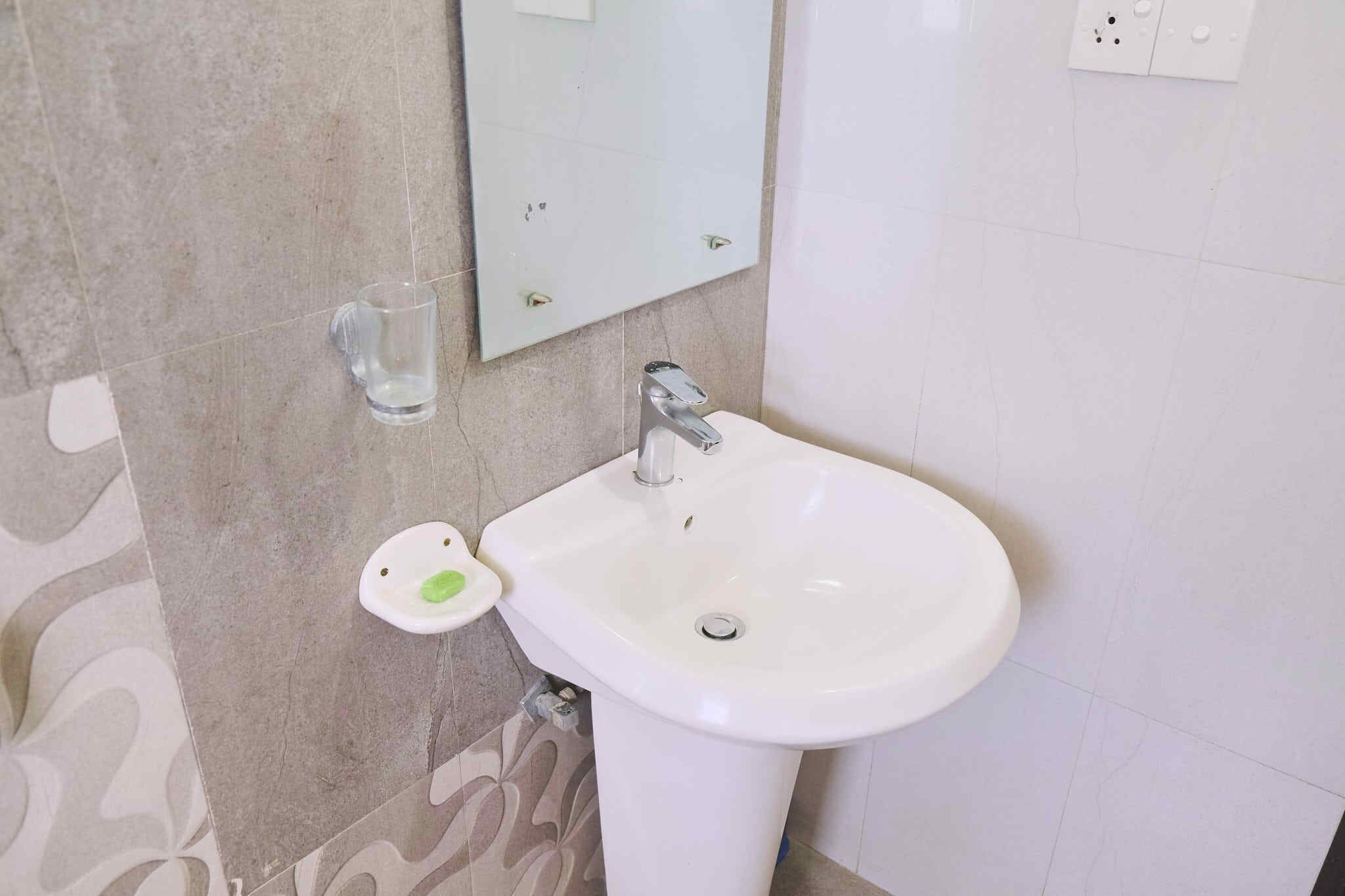 Een badkamer met een witte wastafel, een spiegel en een zeepbakje.