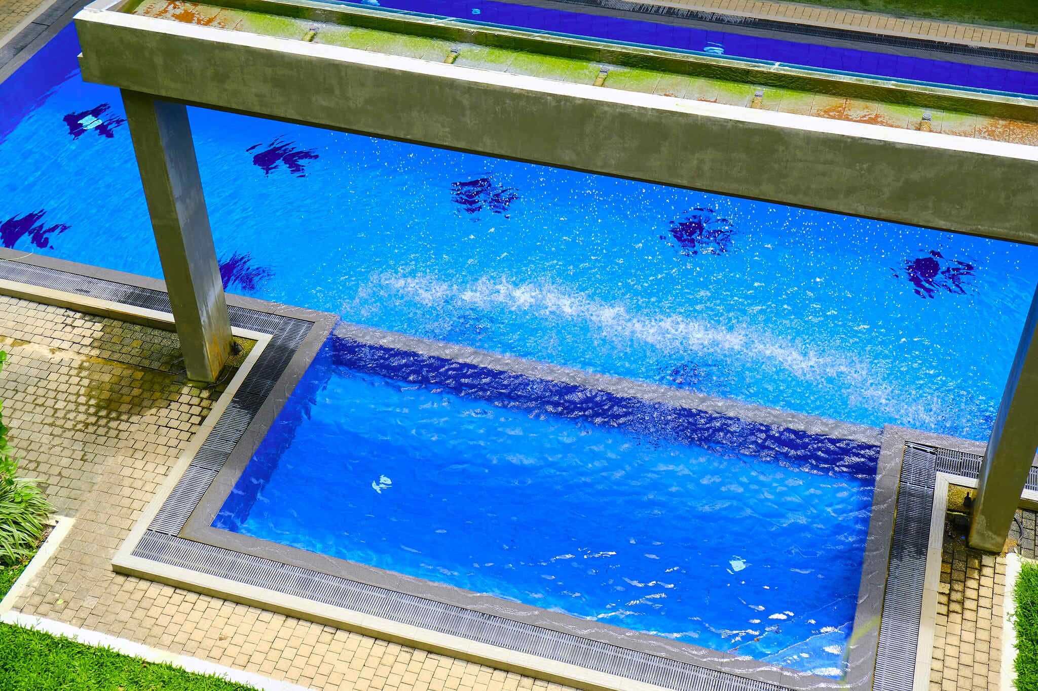 A swimming pool with a clear water surface, surrounded by a tiled deck and a metal safety railing.