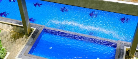 A swimming pool with a clear water surface, surrounded by a tiled deck and a metal safety railing.