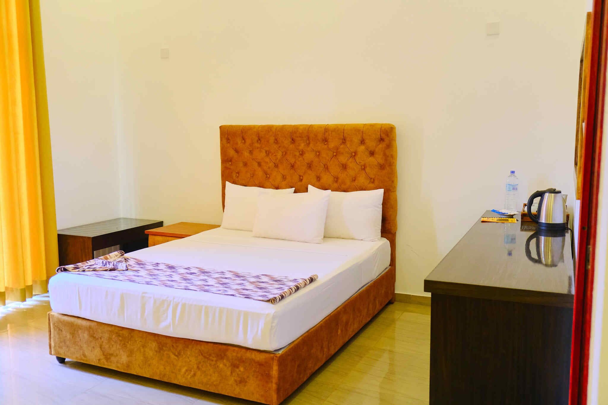Habitación de hotel con una cama grande, una mesita de noche y un escritorio con hervidor.