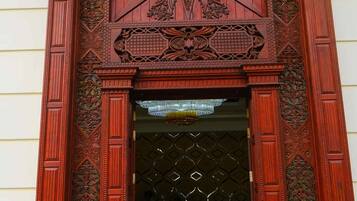 A wooden entrance with intricate carvings and a yellow carpet leading up to a door with a geometric pattern.