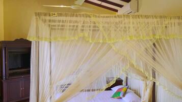 A room with a bed under a canopy, a ceiling fan, and a television on a stand.