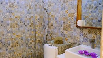Ein Badezimmer mit gemusterten Fliesen, einer Dusche, einem Waschbecken mit Handtuch und einem Spiegel.
