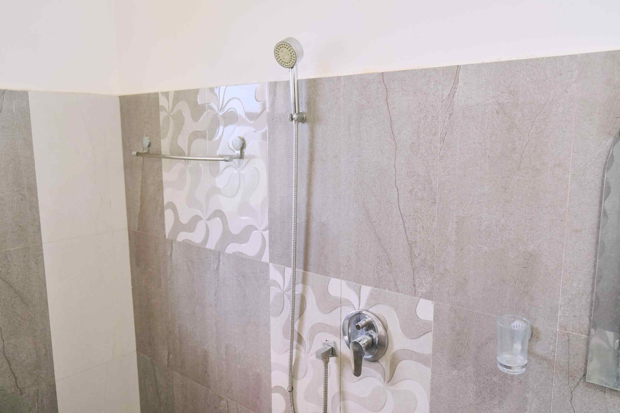 A shower area with a handheld showerhead, a wall-mounted faucet, and a glass soap dispenser.