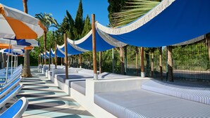 A poolside area with lounge chairs and umbrellas, surrounded by palm trees and a fence. - tent Mojito Suites (Calvia)