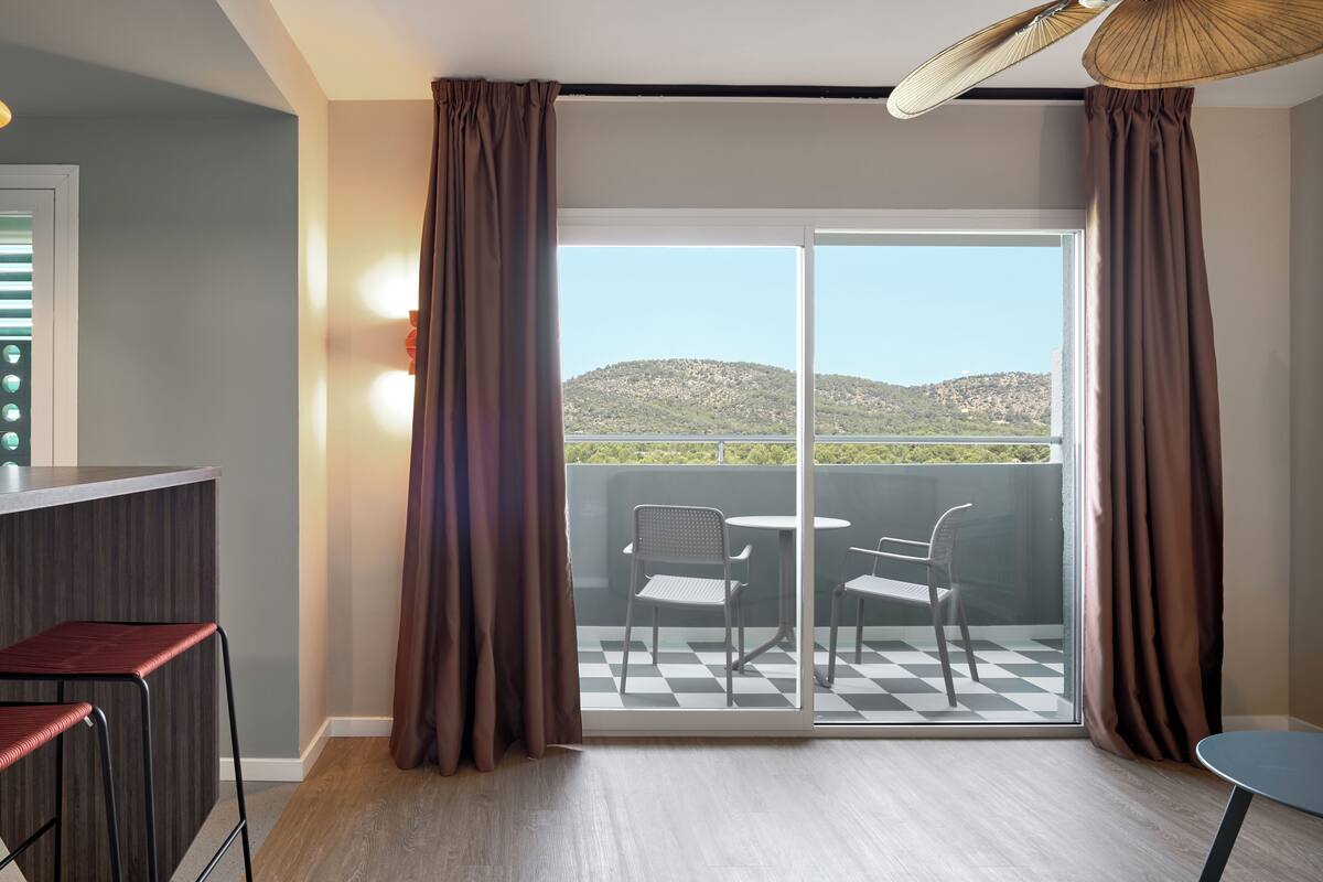 A room with a balcony, a checkered floor, and a view of hills.